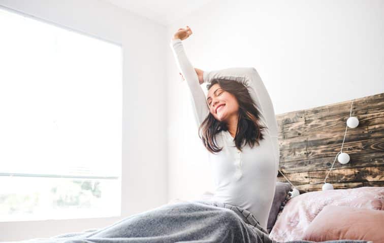 woman rising out of bed and stretching after good sleep hygiene